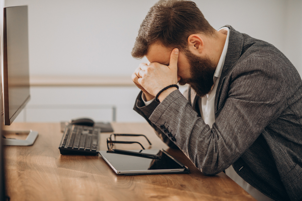 A businessman presses his hands over his eyes at his desk.