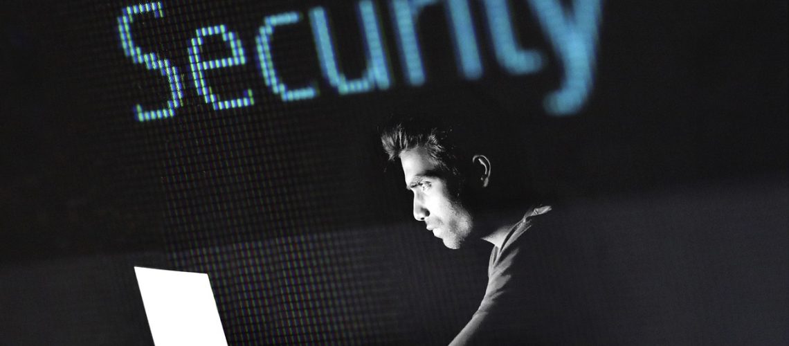 a man in the dark staring at a computer screen to represent the imminent threat of a cyber hack without cyber insurance