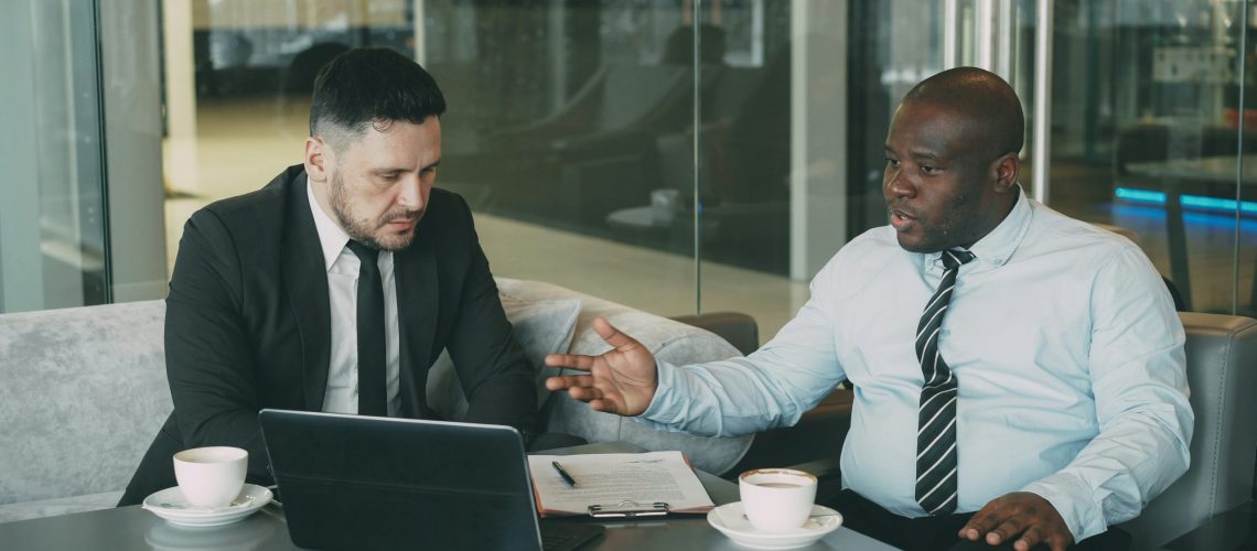 two businessmen having a tense discussion beside an open laptop